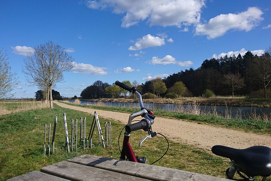 Fahrrad am Kanal Ein Blick auf den Elbe-Lübeck-Kanal. Im Hintergrund ist ein Fahrradlenker, angelehnt an einen Tisch zu sehen. Blauer Himmel mit Schäfchenwolken